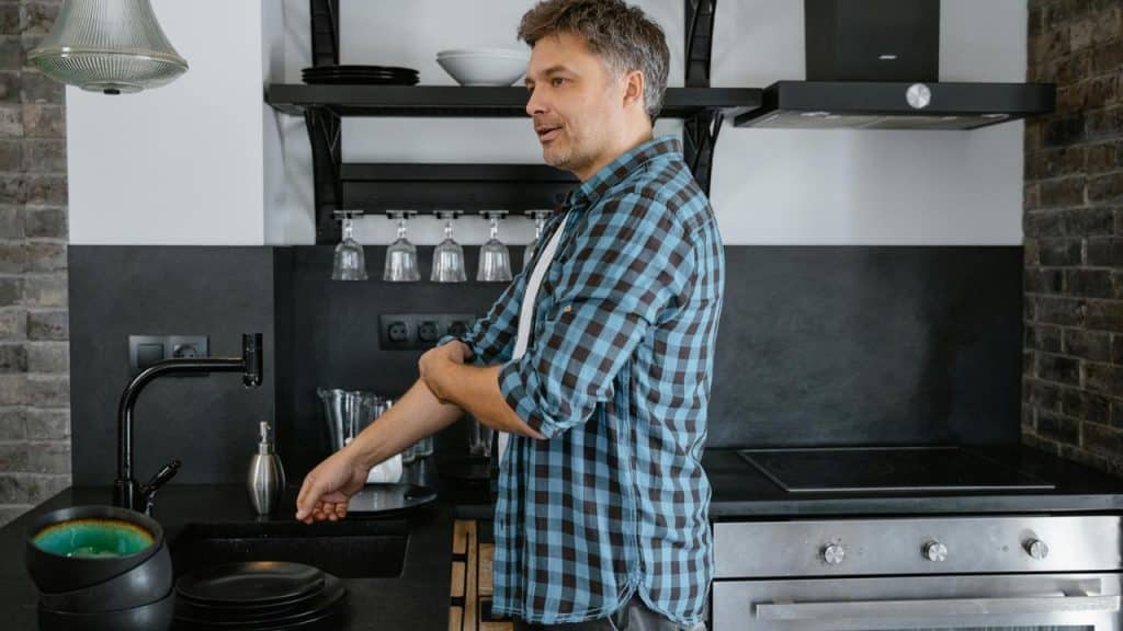 A person standing in a kitchen rolling up their sleeve near the sink.