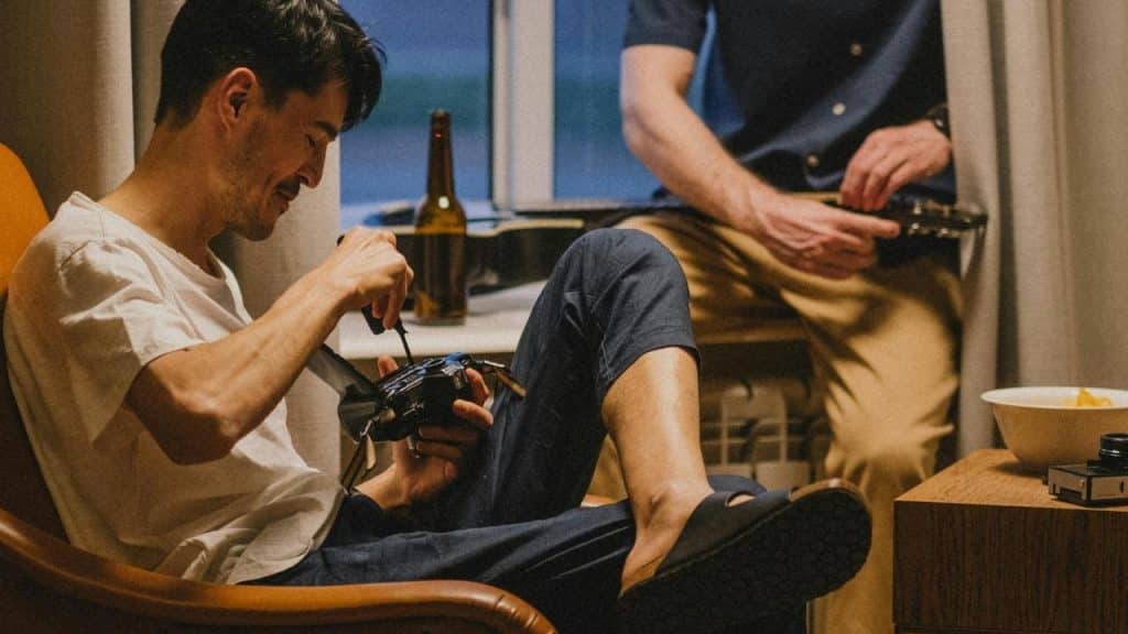 A person sitting in a chair fixing a camera while another sits nearby.
