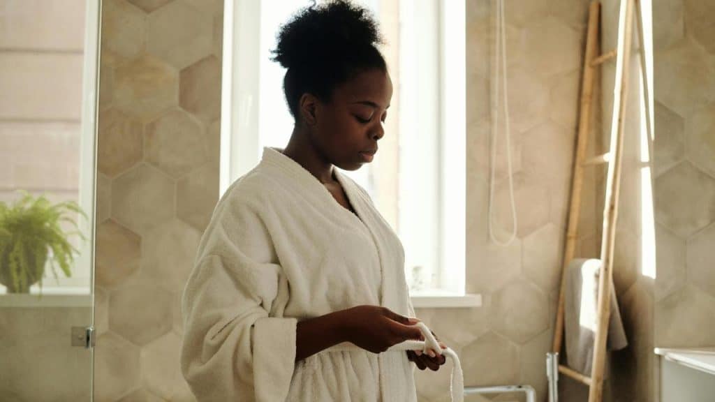A woman in a white bathrobe standing in a bathroom.