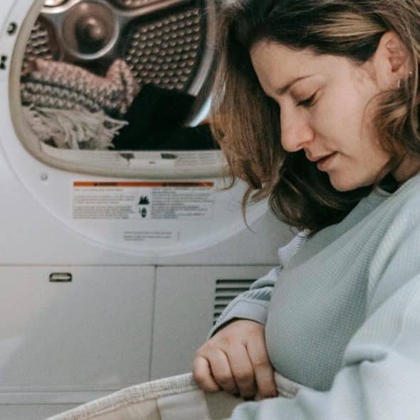 A woman loading clothes into a dryer in a laundry room.