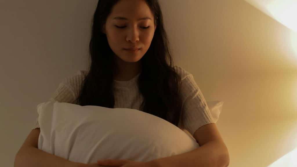 A woman sitting in dim light while hugging a pillow.