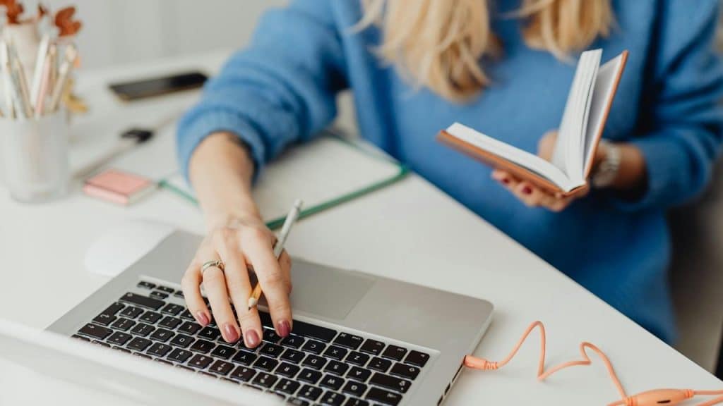 A woman working at a desk with a laptop and notebook.
