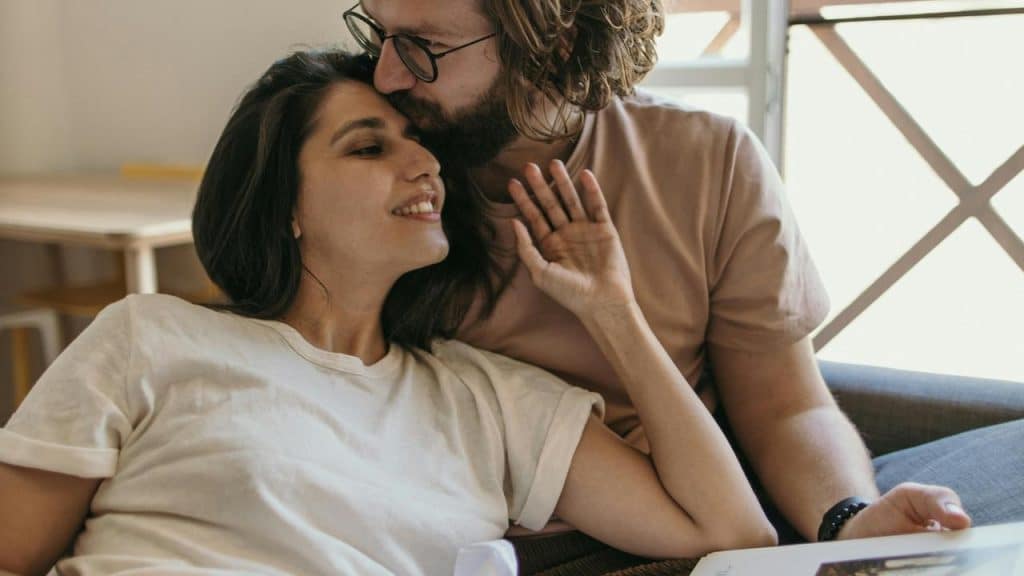 A man kissing a woman on the forehead as they relax together on a couch.