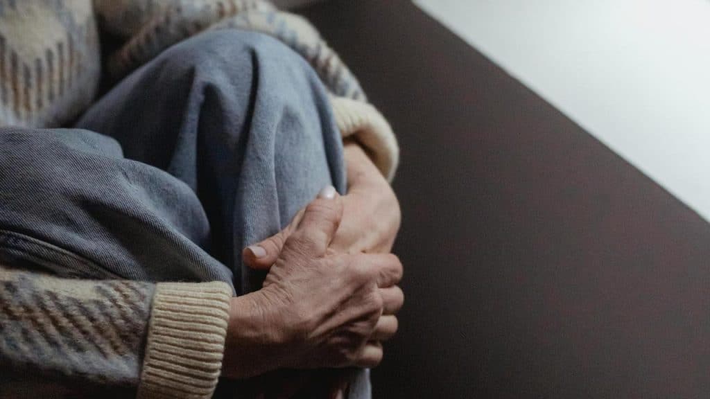 A person sitting with their knees drawn up, wearing a sweater and jeans.