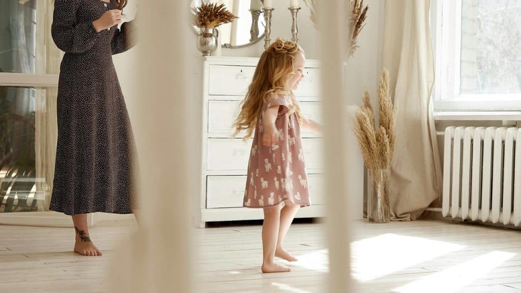 A little girl playing indoors near a woman in a long dress.