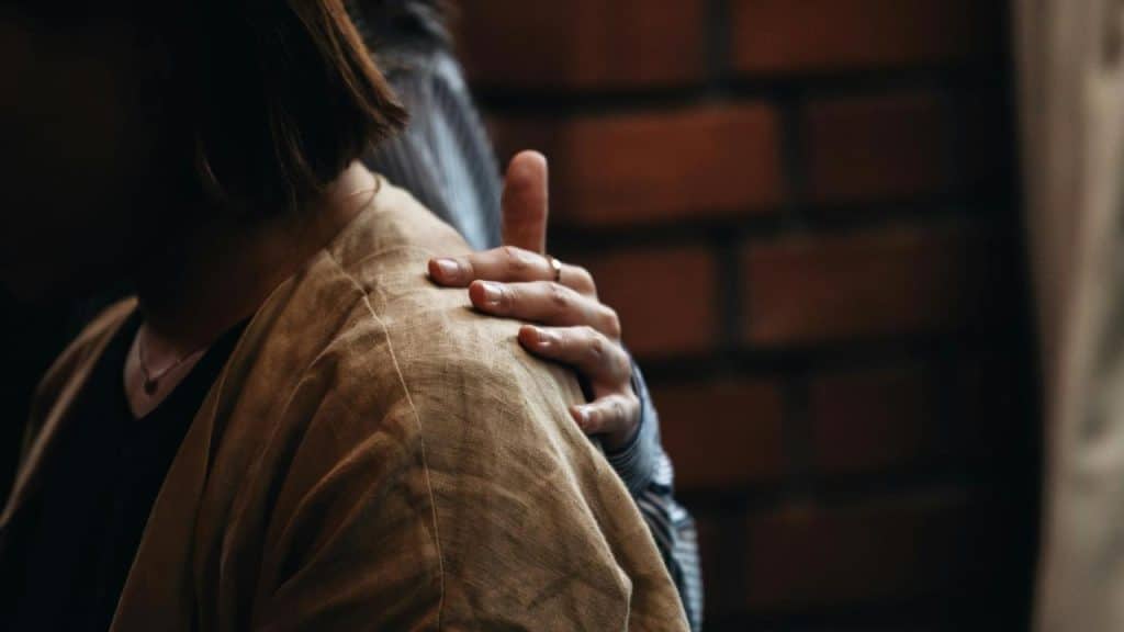 A person comforting another by placing a hand on their shoulder.