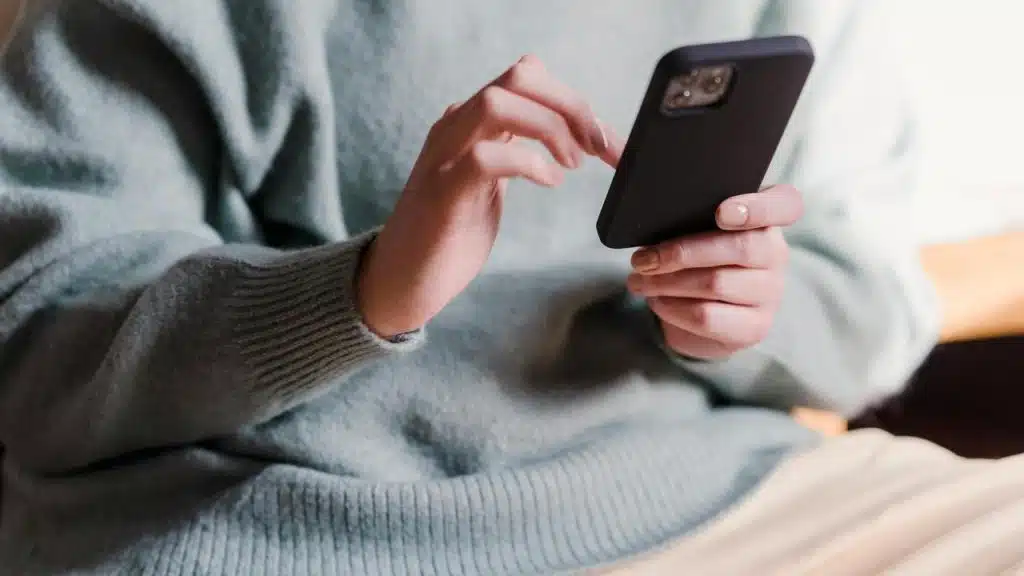 A person wearing a light sweater using a smartphone.