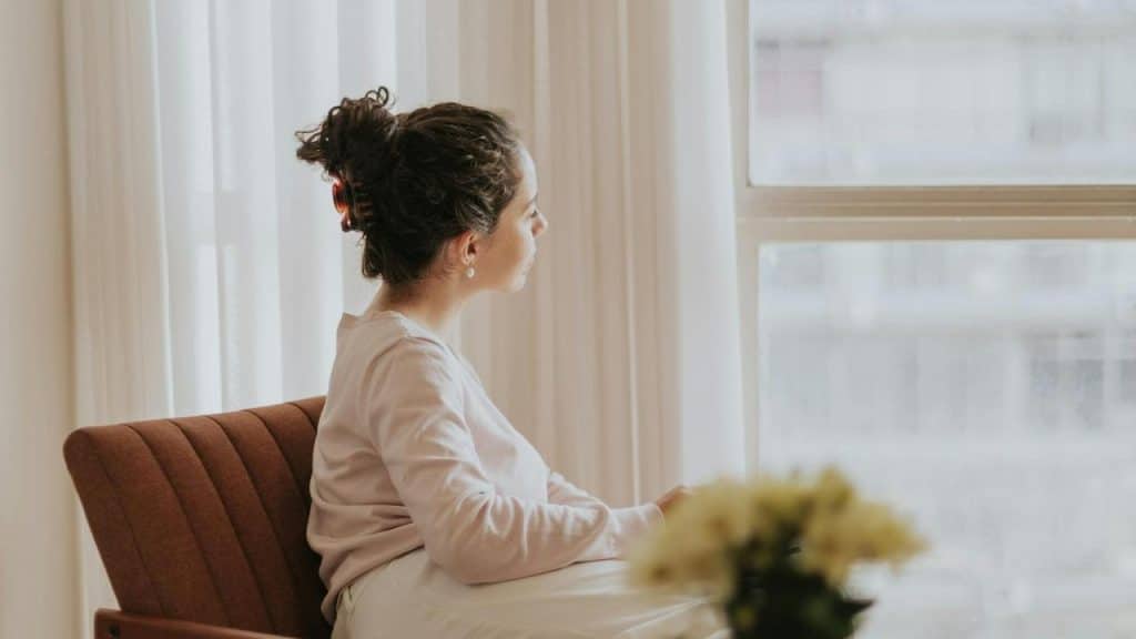 A person sitting on a chair and gazing out of a window thoughtfully.