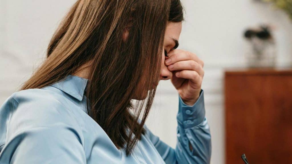A person in a blue shirt rubbing their eyes in frustration or fatigue.