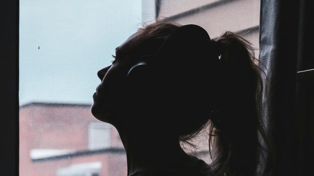 A person wearing headphones sitting by a window and looking outside.