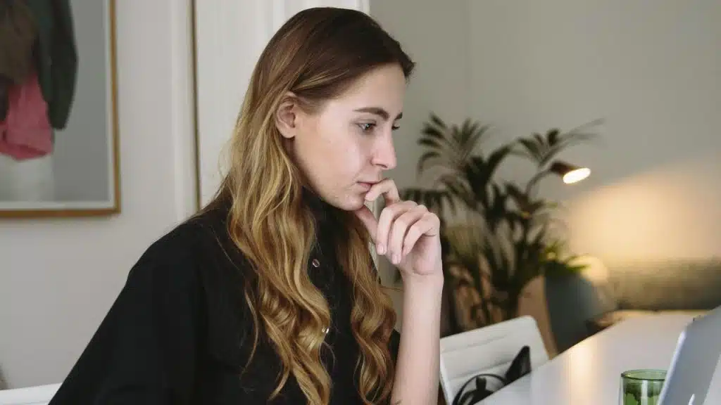 A person sitting at a desk and looking thoughtfully at a laptop screen.