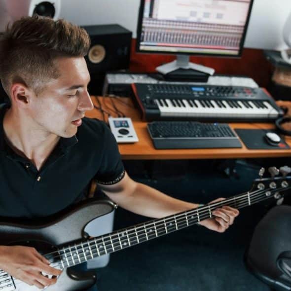 A young musician records bass guitar indoors in the studio.