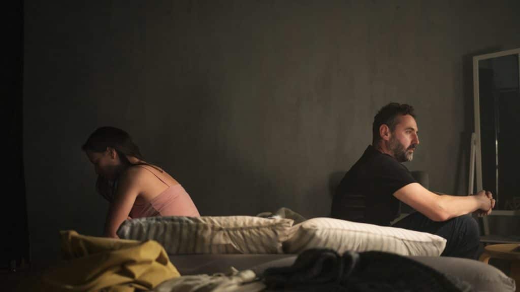 A man and a woman sitting separately on a bed.