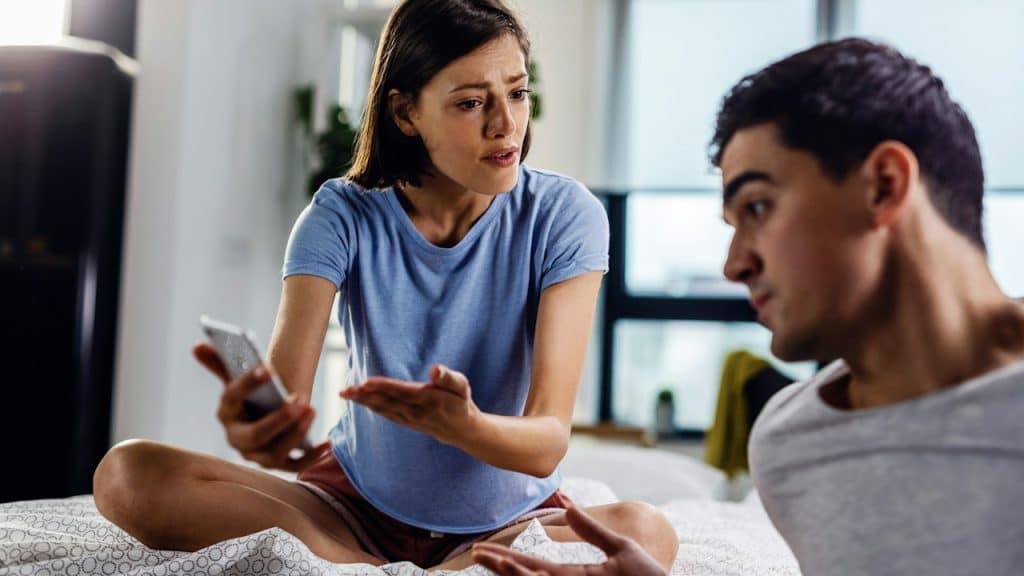 A disappointed woman arguing with her boyfriend about a text message on a mobile phone.