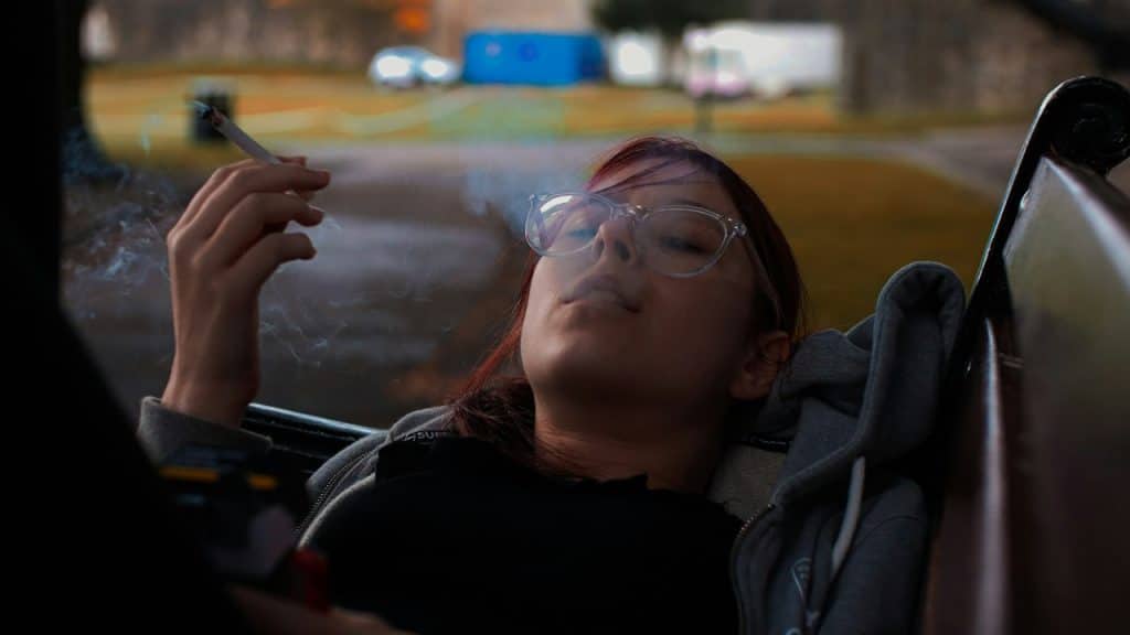A woman smoking while lying on a bench.