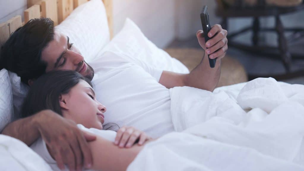 A man using phone while his wife is sleeping with him