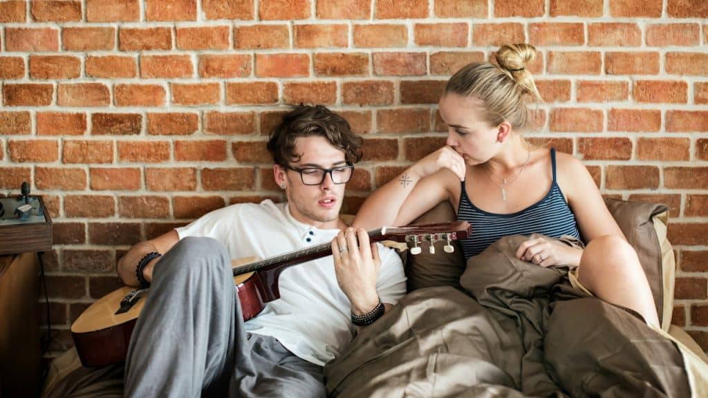 A man is playing guitar while his girlfriend is listening silently.