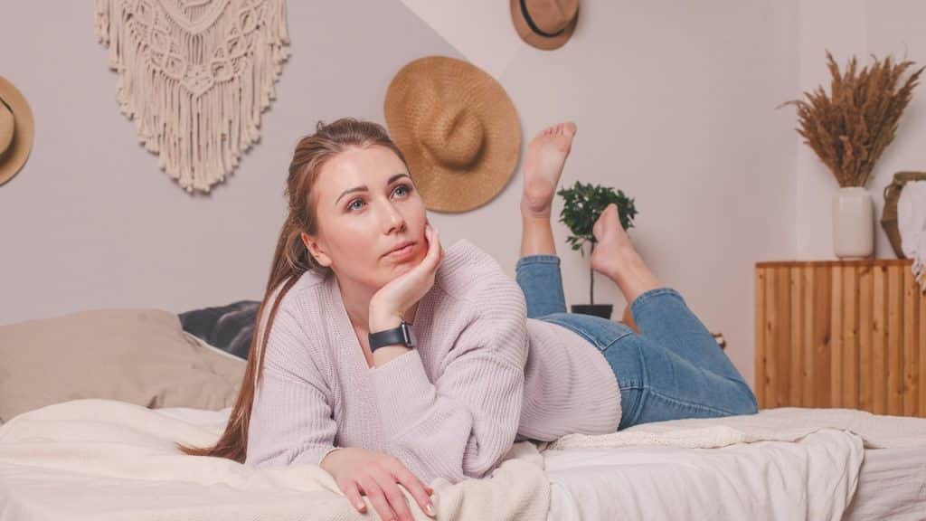 A thoughtful woman lying on a bed holding her face with her hand.
