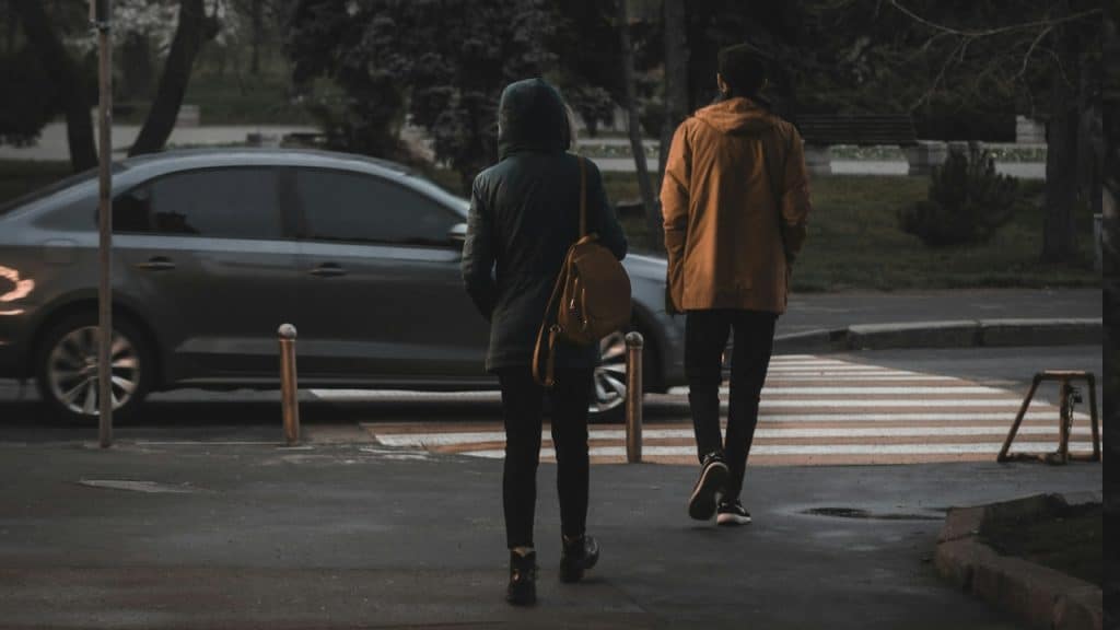 A man and a woman walking near a gray car.