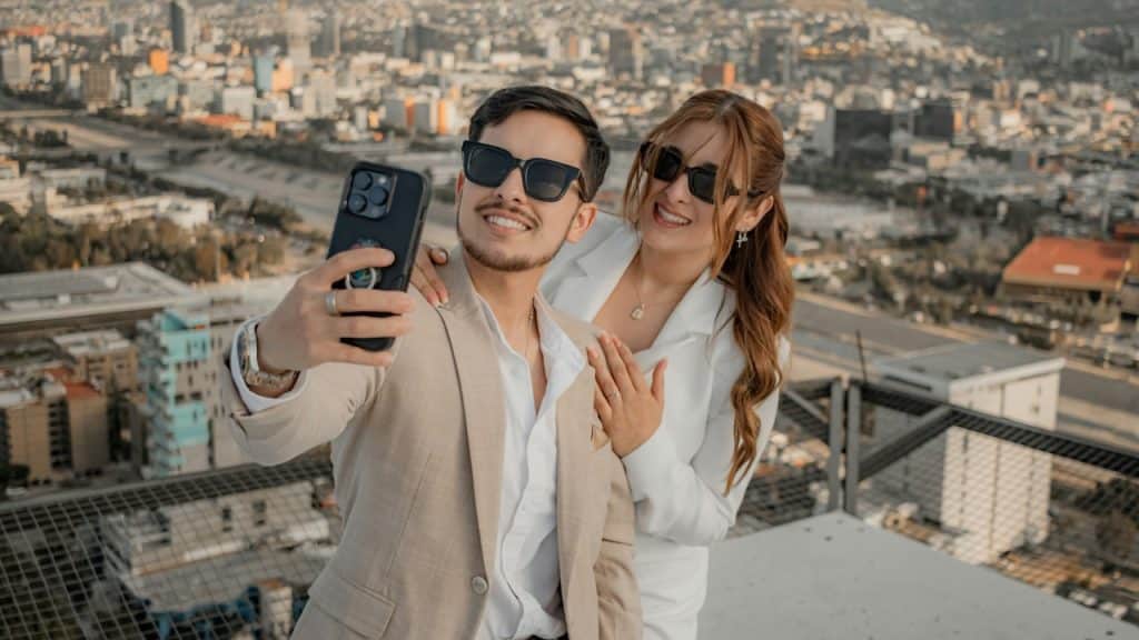 A man and woman taking a selfie at a rooftopwith a cell phone.