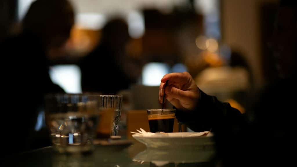 A male hand mixing coffee with a spoon while a woman is sitting separately.