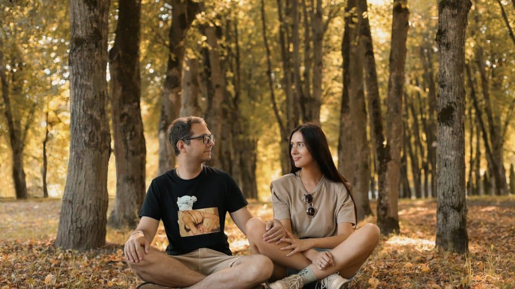 A man and a woman sitting on the ground in a forest.