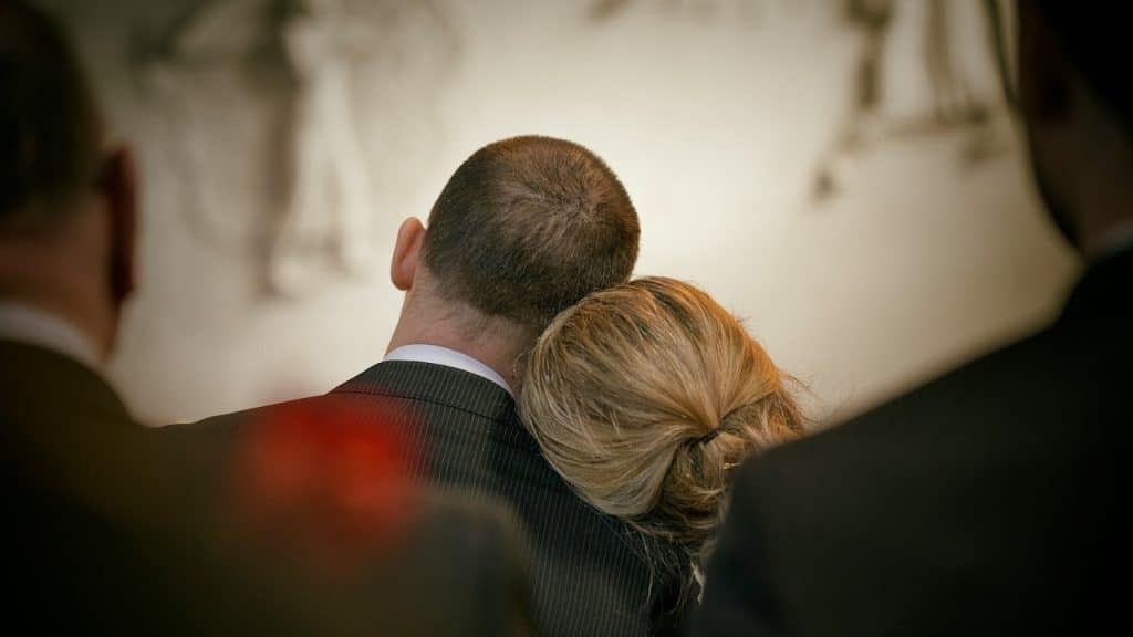 A woman resting her head on a man's shoulder, viewed from behind, in a formal setting.