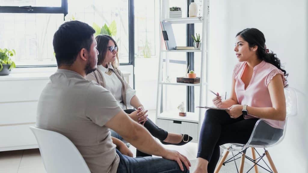 A therapist or counselor speaking with a couple in an office setting.