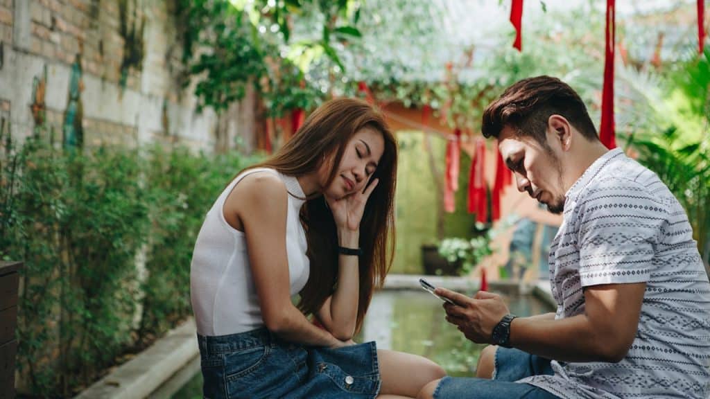 A wife waiting for her husband, who is busy using his phone.