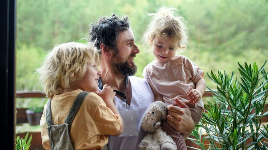 Smiling man holding a young girl and standing next to a young boy outdoors.