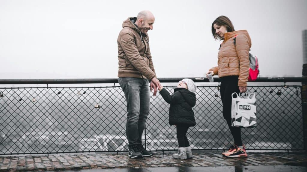 A man, a woman, and a small child stand on a bridge or platform on a cloudy day.
