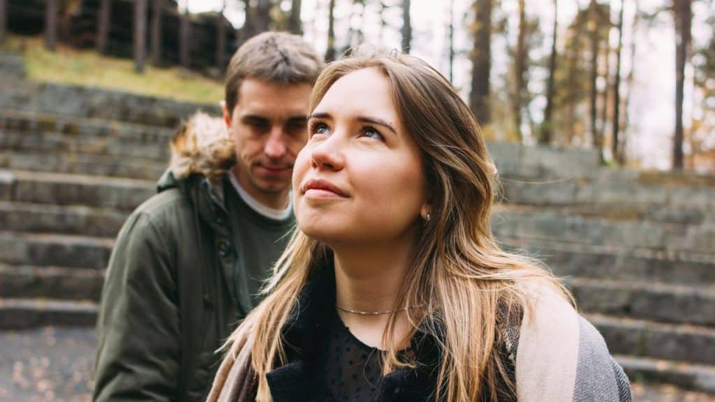 A smiling woman looking up, with a serious man standing behind her on stone steps outdoors.