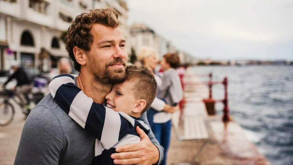 A happy father and son hugging on a city boardwalk by the waterfront.