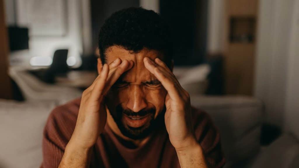 A distraught man holding his temples with both hands, looking stressed and in pain.