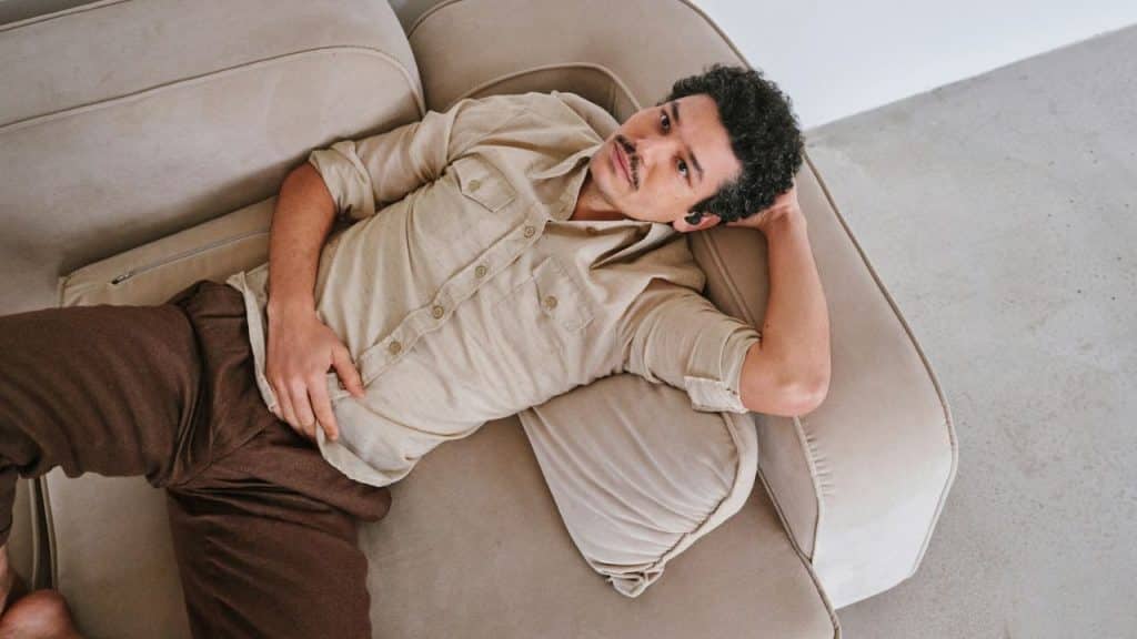 A man with a mustache lying back on a light-colored sofa looking upward.