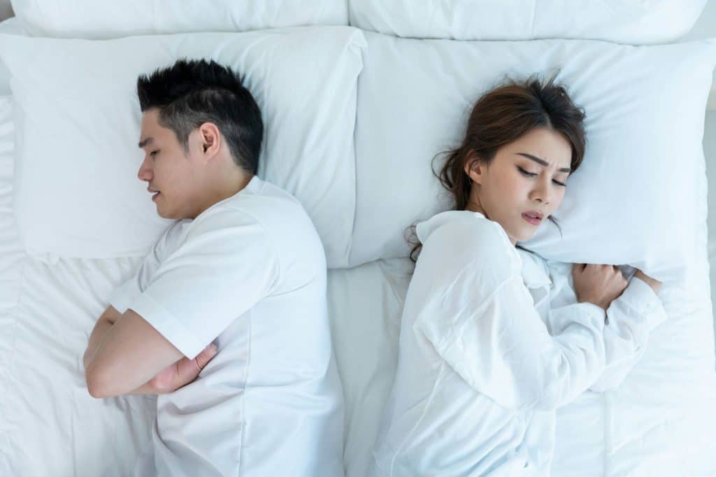 A man and woman laying in bed and facing opposite directions