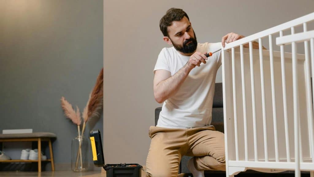 A man assembling a white crib with a screwdriver.