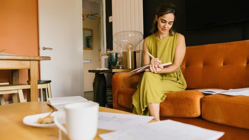 A woman sitting on a couch writing in a notebook in a cozy living room.