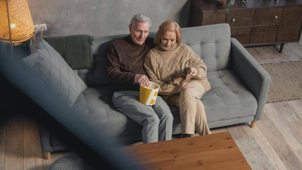 A senior couple sitting on a couch eating popcorn together.