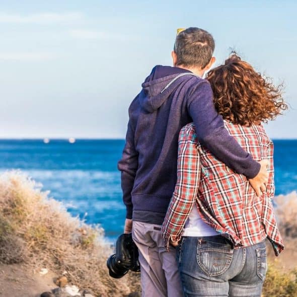 A couple standing together while admiring the beach view.