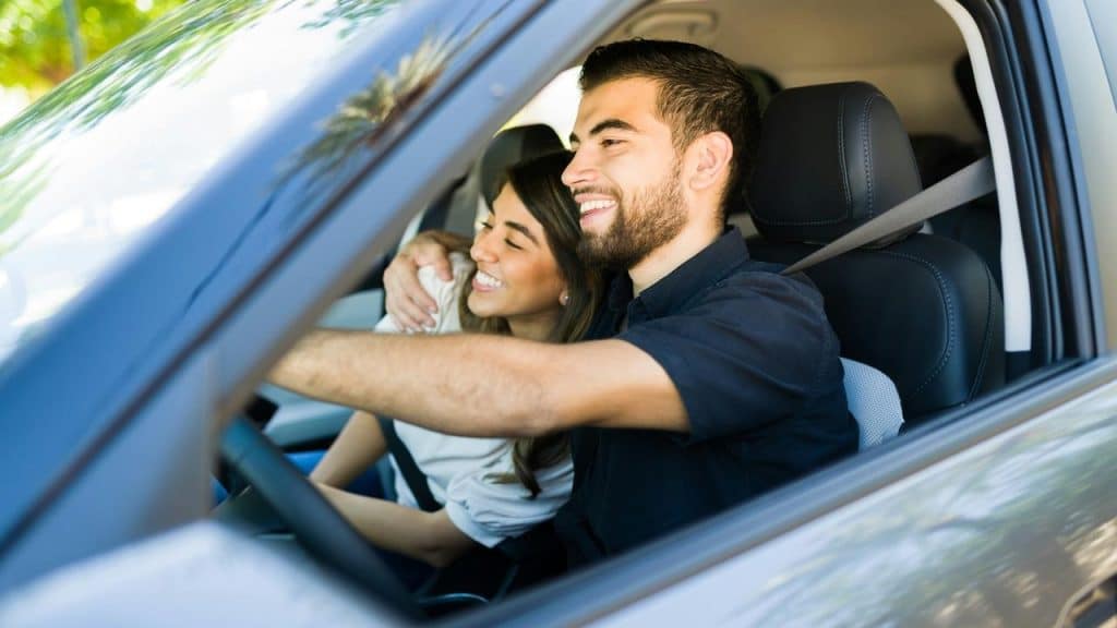 A couple inside a car driving and hugging each other.
