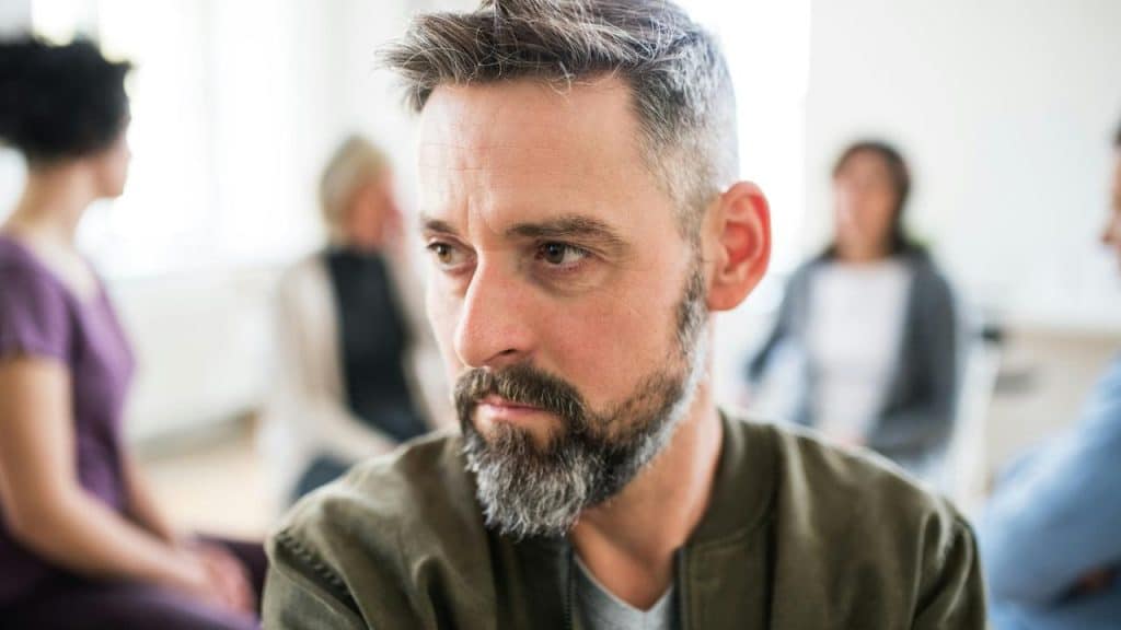 A man with a thoughtful expression as he sits in a therapy session.