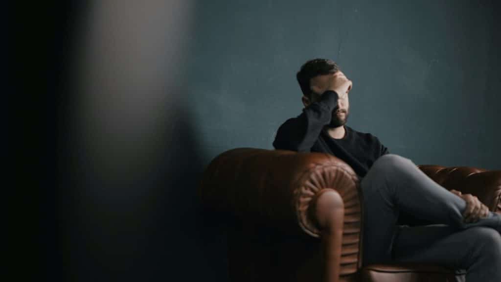 A distressed man is sitting in a leather armchair with his hand covering his face.