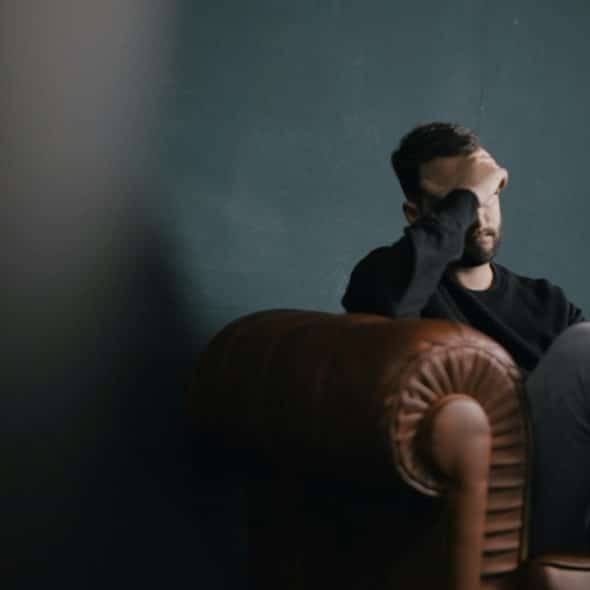 A distressed man is sitting in a leather armchair with his hand covering his face.