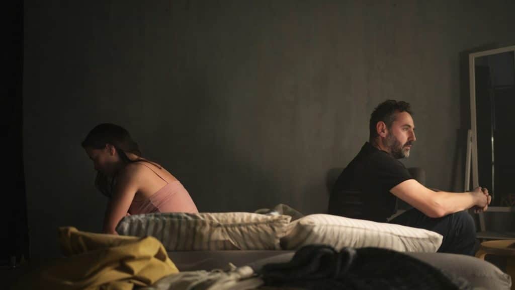 A couple sitting apart from each other with their backs to each other on a bed and refusing to talk.