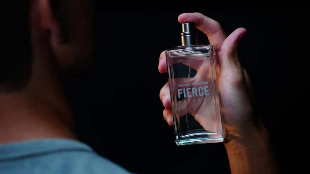 Close-up of a hand holding a bottle of Abercrombie & Fitch Fierce Cologne against a dark background.