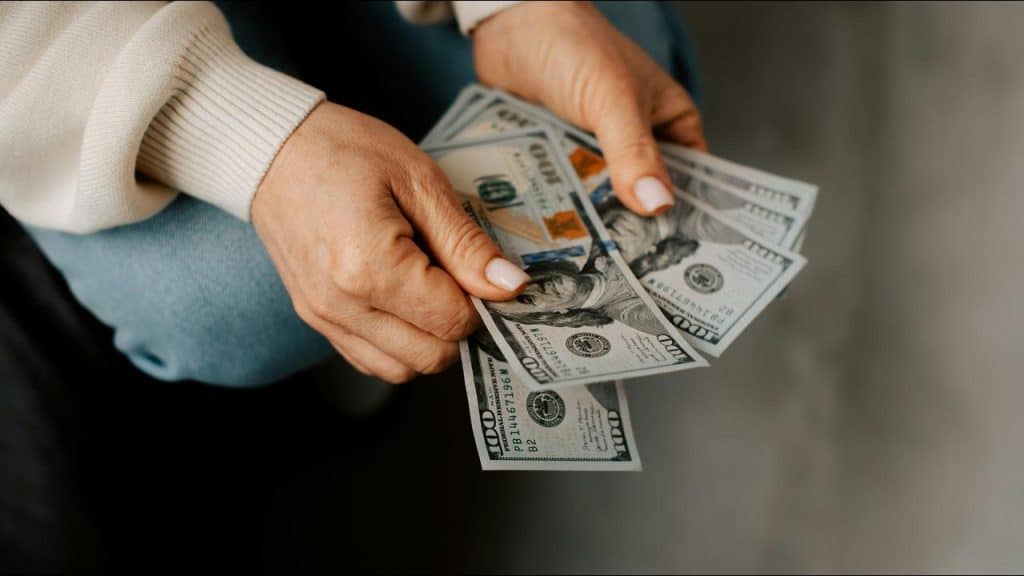 A close-up of hands holding a stack of crisp hundred-dollar bills.