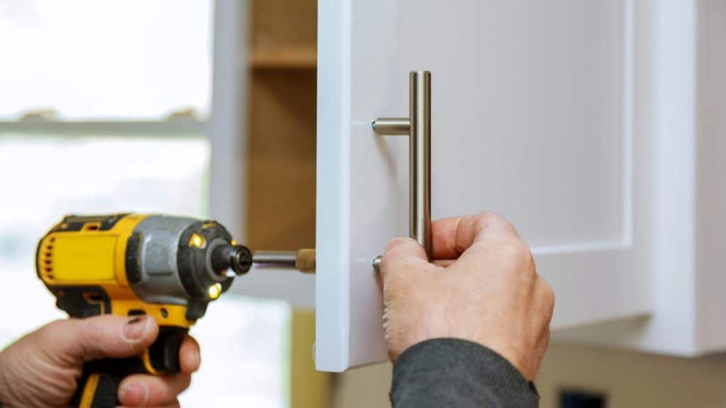 A person using a drill to attach a handle to a cabinet door at home.