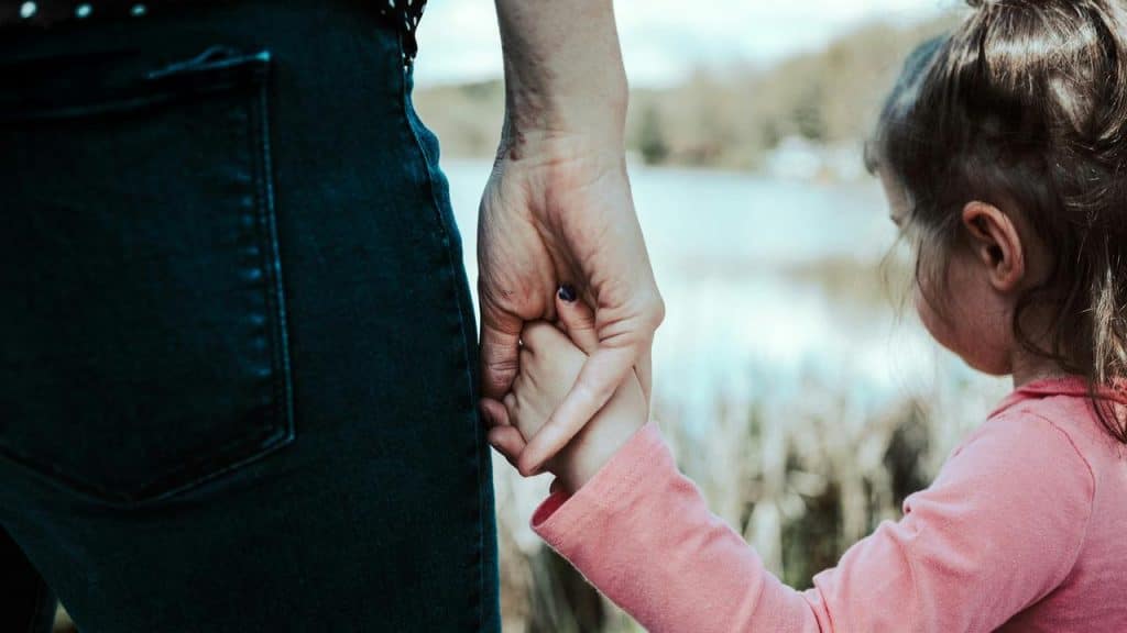 A child walking hand in hand with an adult along a peaceful waterfront.