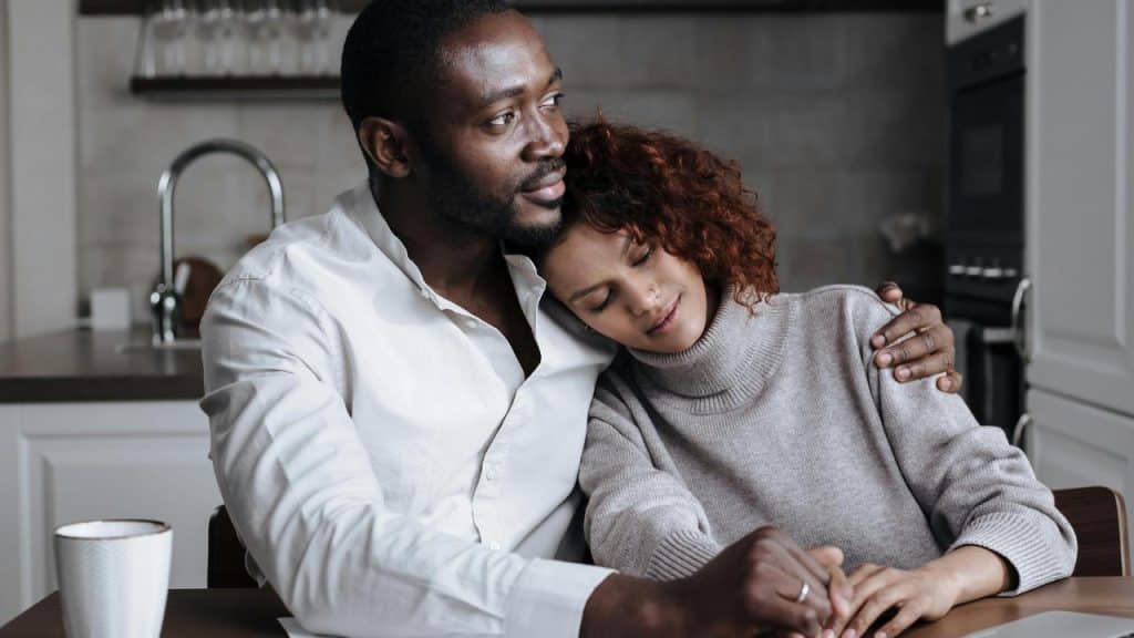 A woman resting her head on her partner’s shoulder while they sit together.